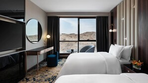A hotel room with a large bed, a desk, a chair, a TV, and a view of the desert.