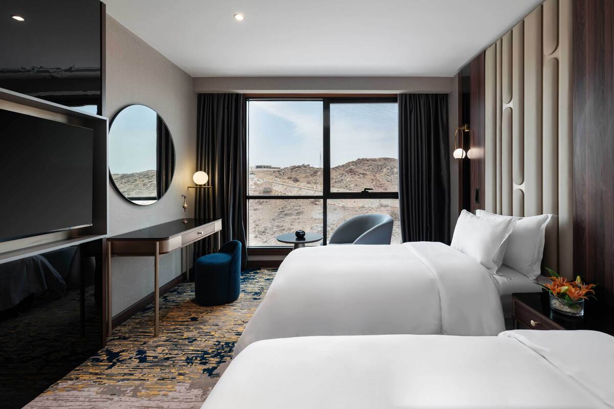 A hotel room with a large bed, a desk, a chair, a TV, and a view of the desert.
