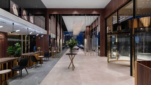 A modern hotel lobby with a central seating area, a reception desk, and a glass elevator.