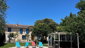 A rectangular swimming pool with a clear blue water surface, surrounded by a tiled deck. There are lounge chairs in blue, red, and white colors. A pergola structure is visible in the background. - Mas in the countryside, authentic Provence! (Châteaurenard)