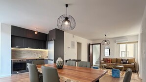 Uma cozinha moderna com armários escuros, uma mesa de jantar de madeira e cadeiras. Há um sofá e uma mesa de centro na sala de estar.