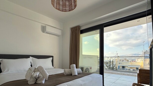Quarto de hotel com uma cama grande, vista da cidade por uma porta de vidro deslizante e um ventilador de teto.