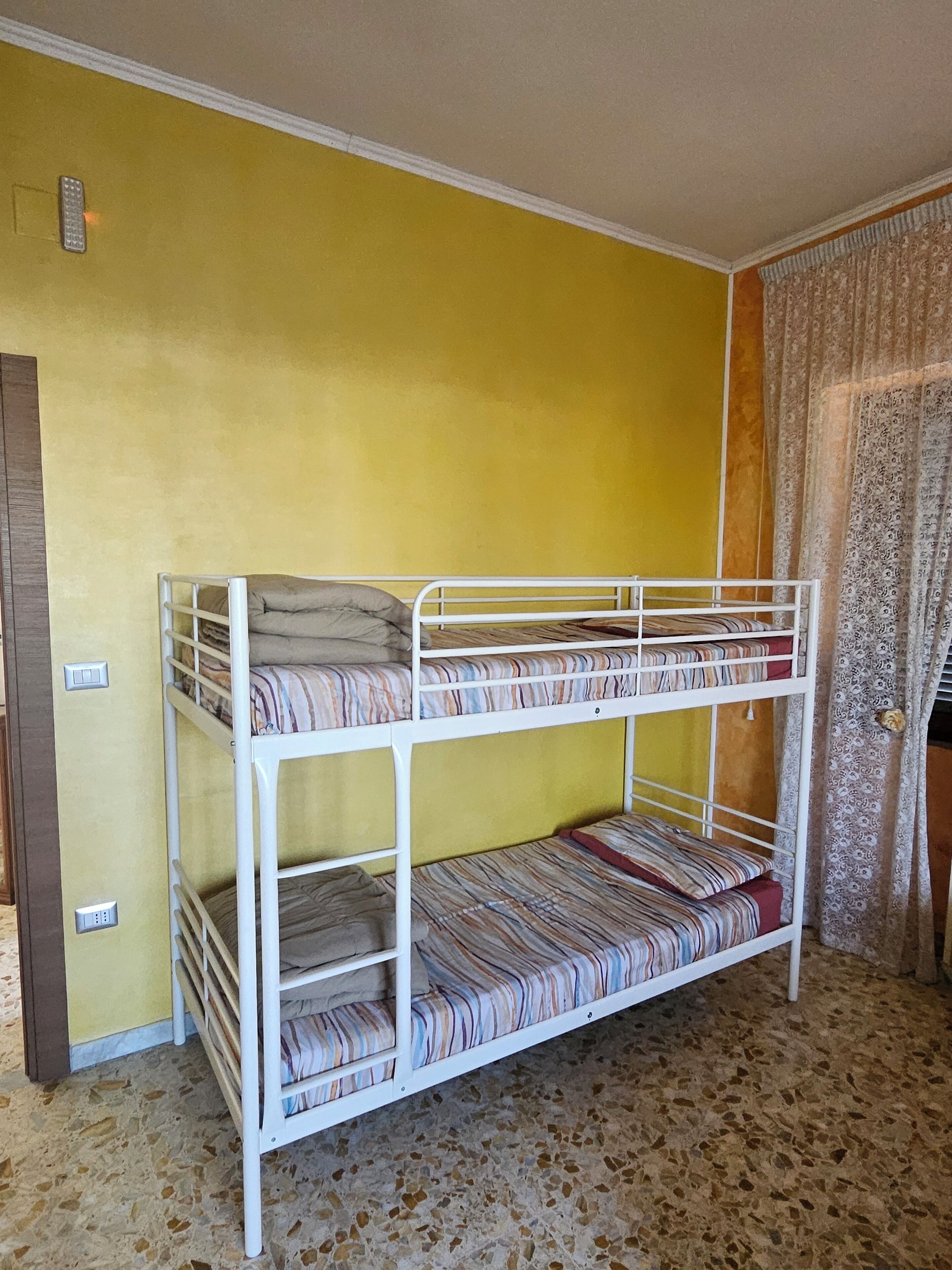 Una cama litera con tres niveles, un colchón estampado y un suelo de baldosas.