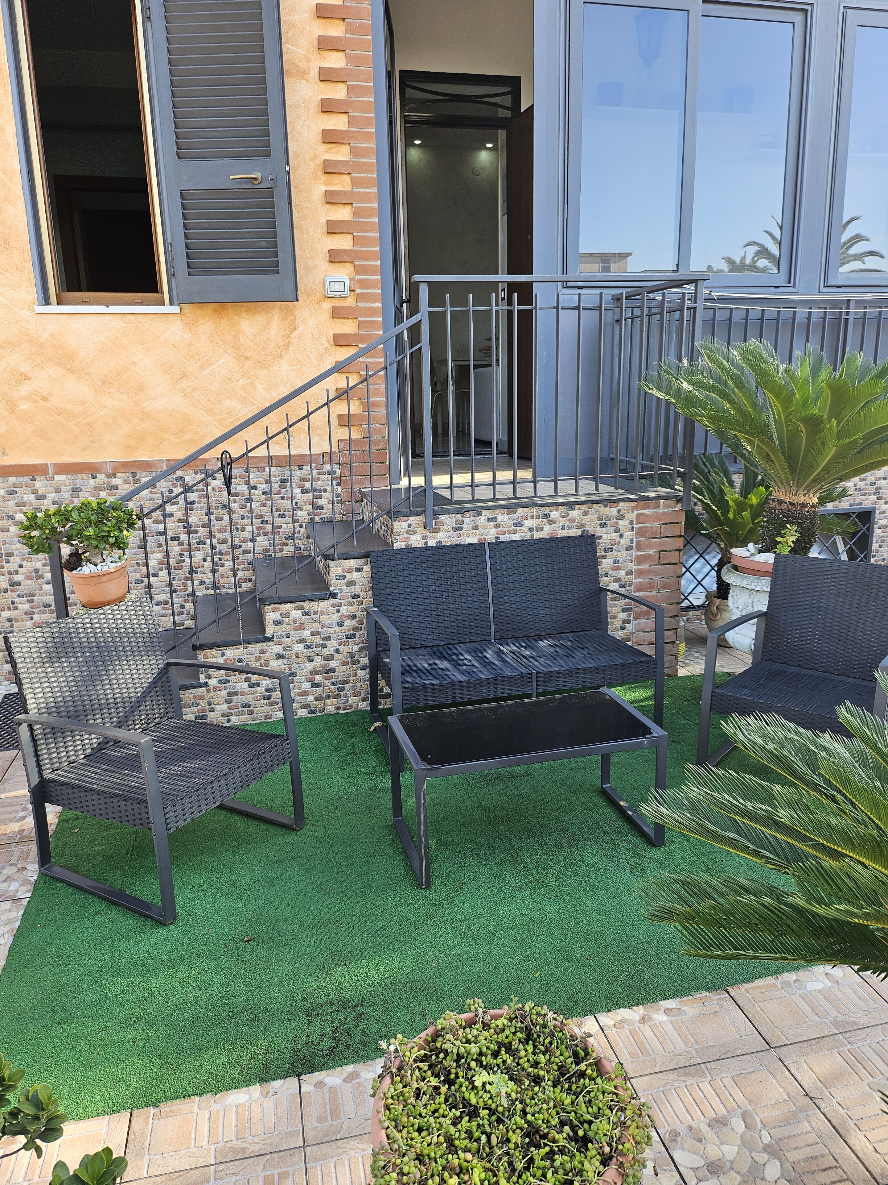 Un patio con mobiliario exterior, una escalera y un muro de ladrillo.