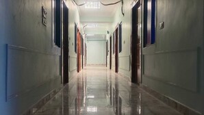 Un long couloir étroit, avec des portes de part et d’autre, un sol en marbre poli et un plafond orné d’un luminaire central.