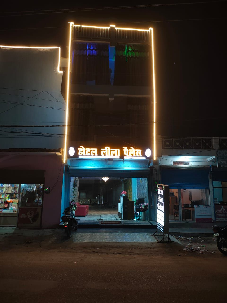 Un edificio con un neon in lingua straniera, una motocicletta parcheggiata davanti e un negozio chiuso con un tendone blu.