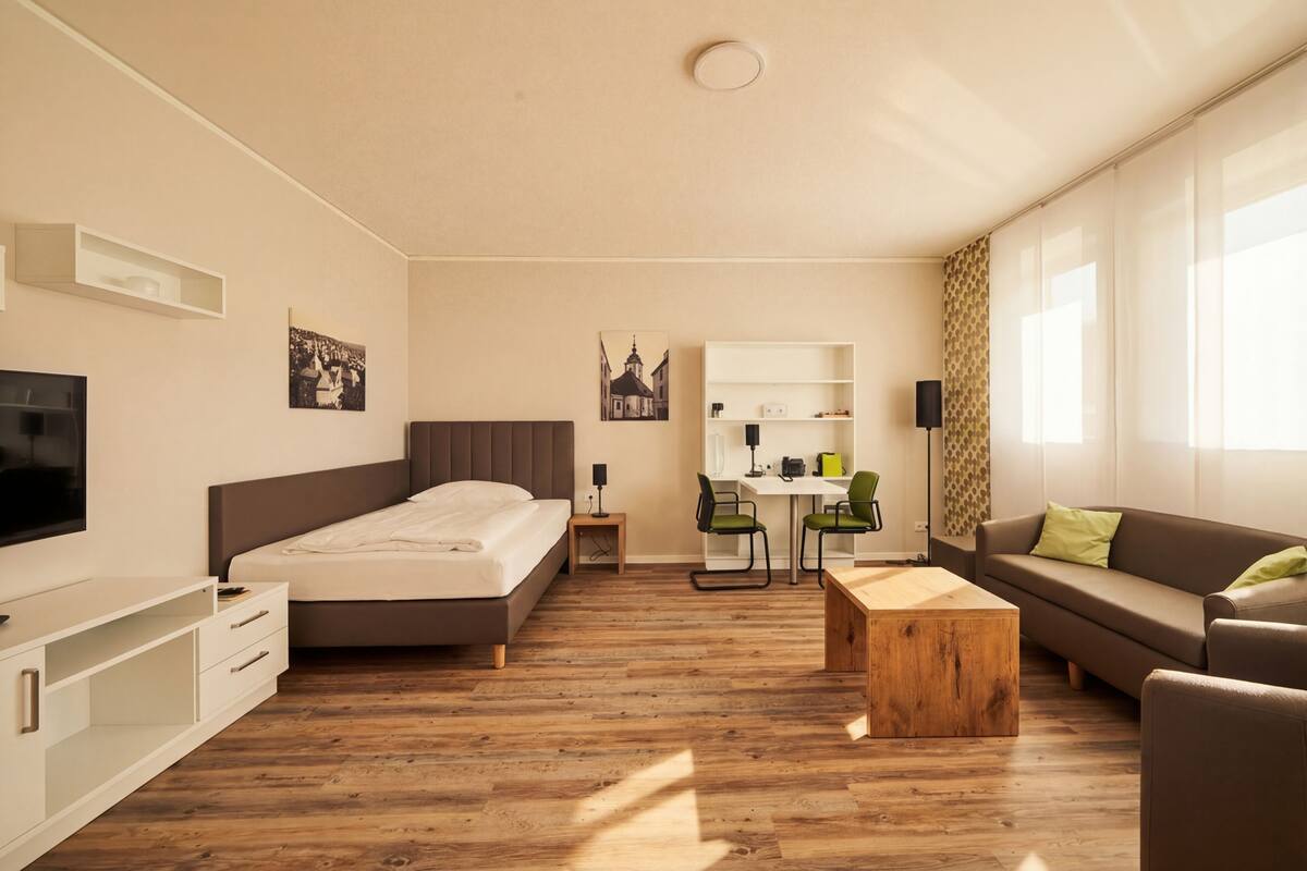 A modern hotel room with a bed, a desk, a sofa, and a TV.