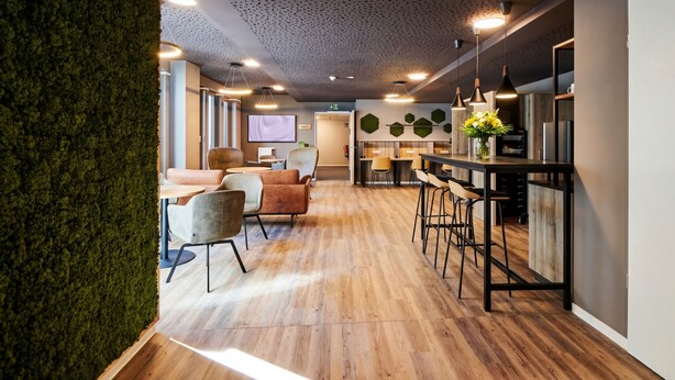 A modern interior with a wooden floor, a bar area with stools, a seating area with chairs, and a green wall. - ADAPT APARTMENT HOTEL Siegen (Siegen)