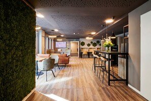 A modern interior with a wooden floor, a bar area with stools, a seating area with chairs, and a green wall. - ADAPT APARTMENT HOTEL Siegen (Siegen)