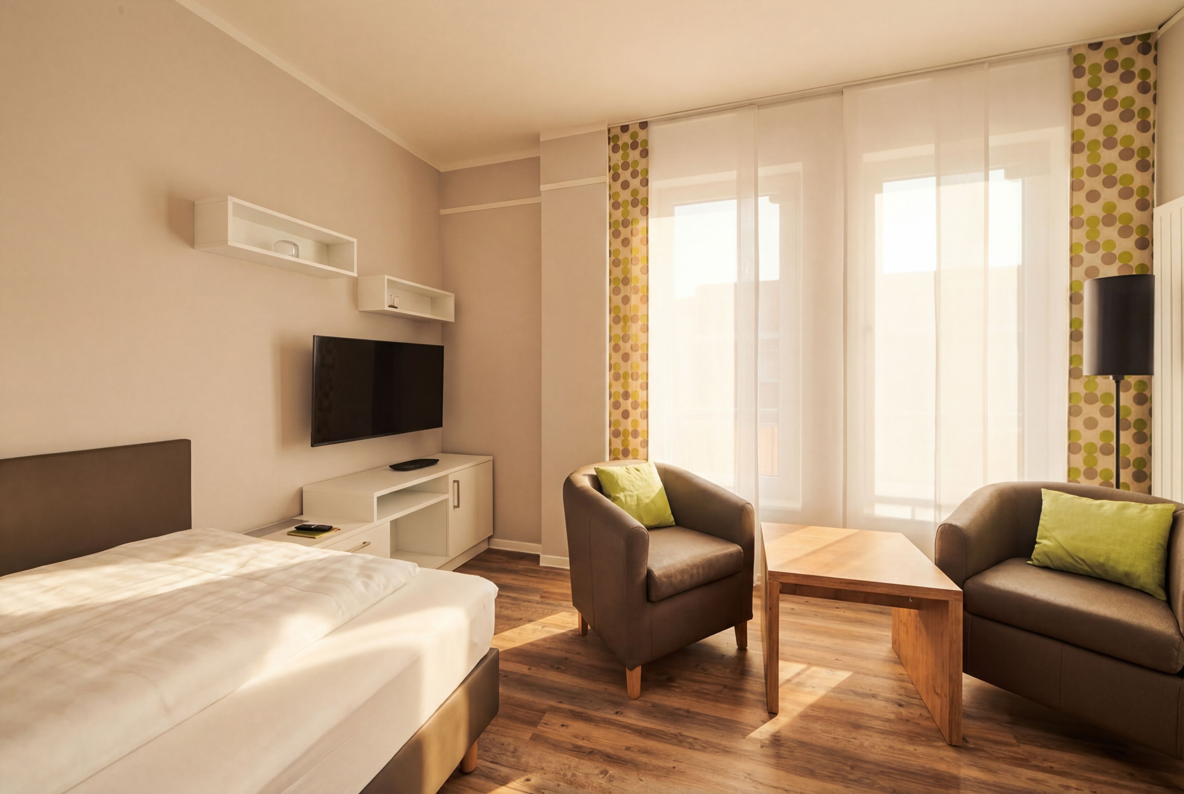 Habitación de hotel con cama, televisión, escritorio, dos sillas, una mesita y ventanas amplias con cortinas translúcidas.