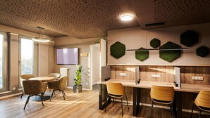A modern office space with a wooden floor, a round table with chairs, a TV on the wall, and hexagonal green wall decorations. - ADAPT APARTMENT HOTEL Siegen (Siegen)