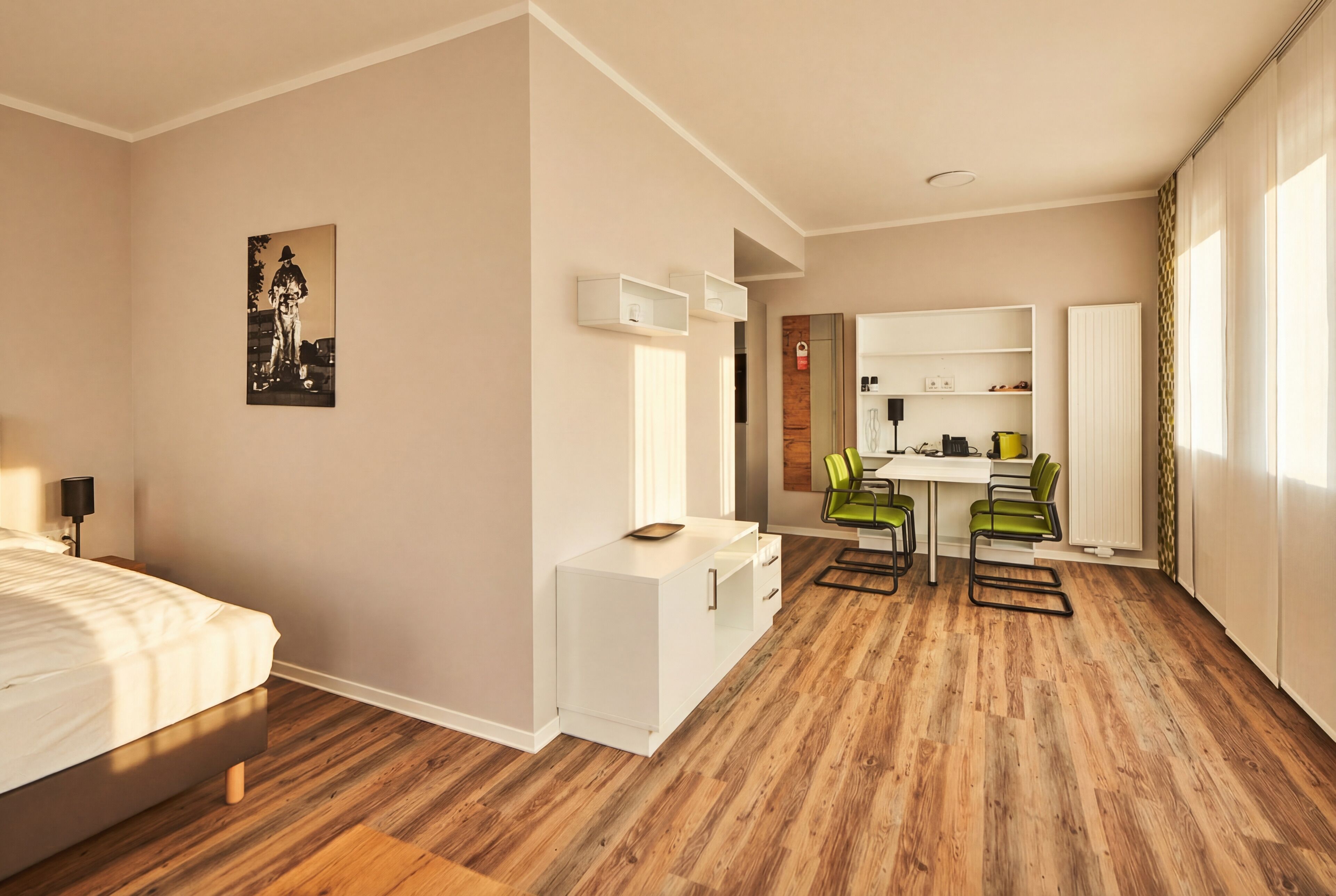 Une chambre d’hôtel comprenant un lit, un bureau, deux chaises, une petite kitchenette et un tableau au mur.