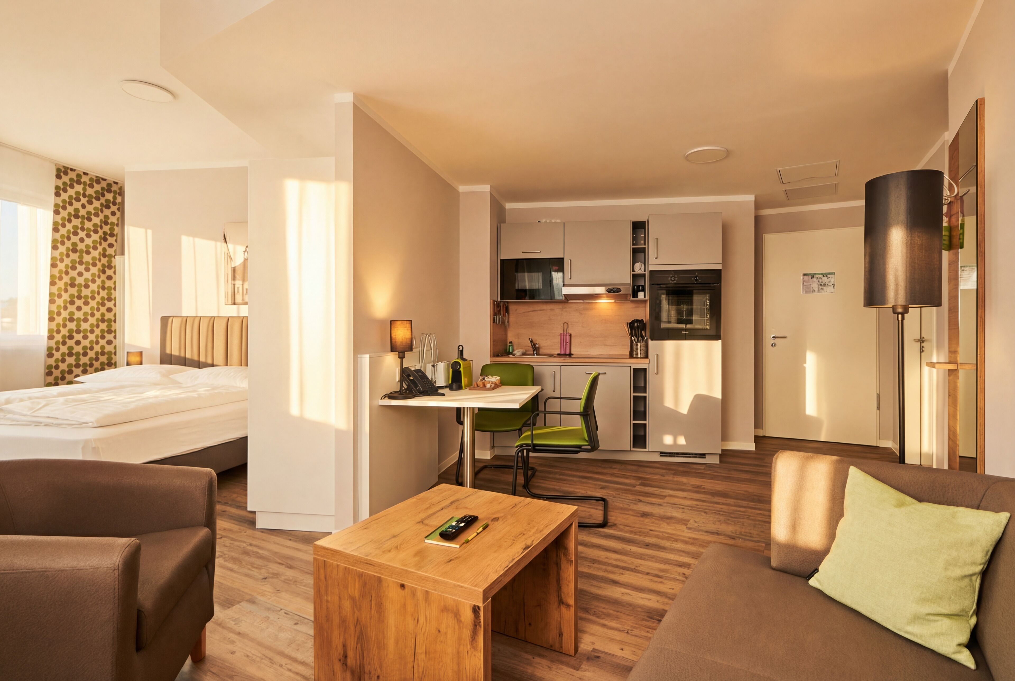 Habitación de hotel con cama, una mesita de madera, sofá, kitchenette y zona de comedor.