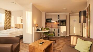 Habitación de hotel con cama, una mesita de madera, sofá, kitchenette y zona de comedor.