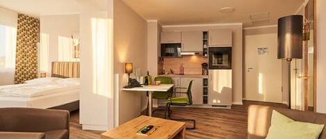 Quarto de hotel com cama, mesa de centro de madeira, sofá, cozinha compacta e área de refeições.