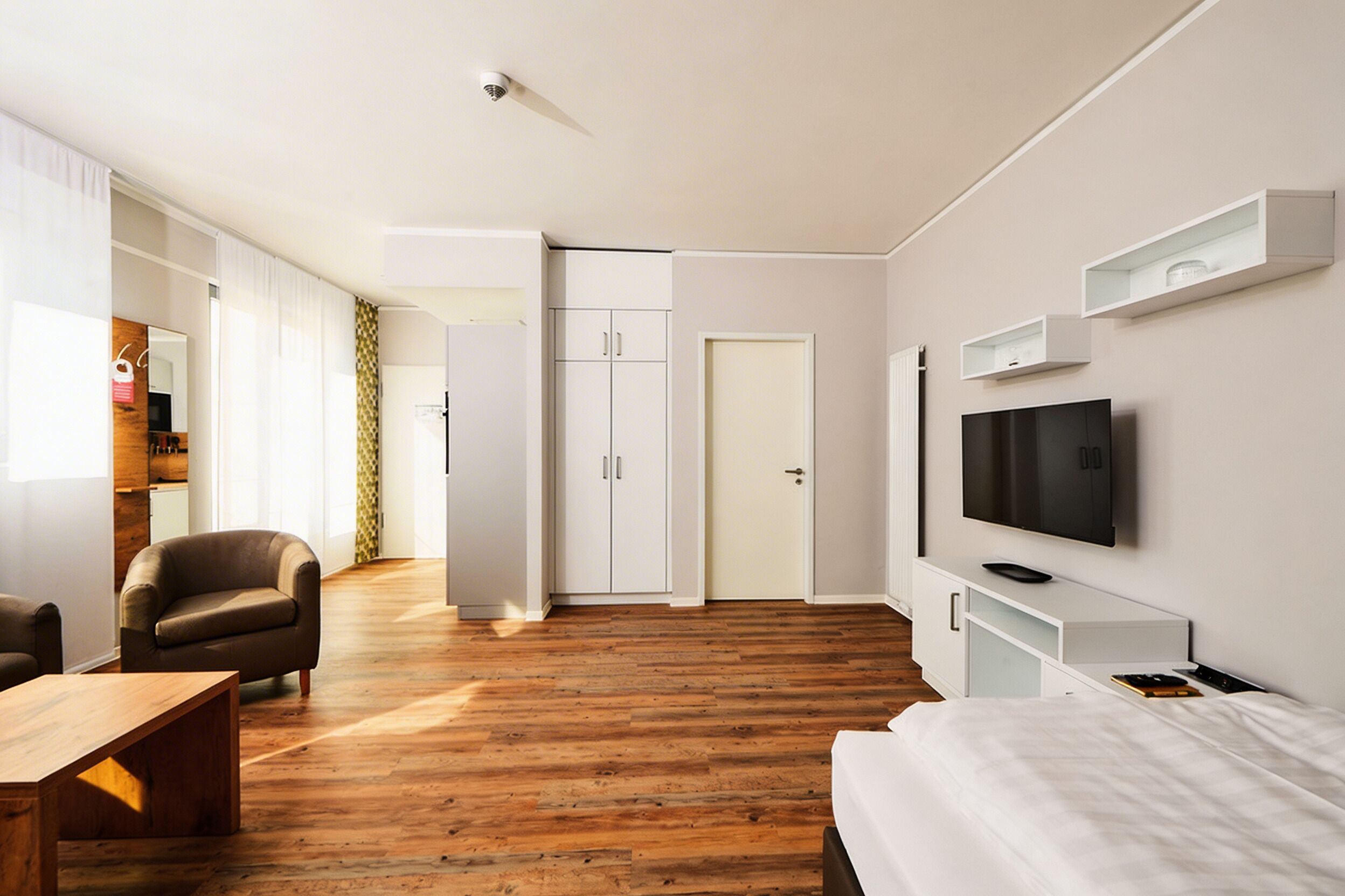 Ein modernes Hotelzimmer mit Holzboden, einem Bett, einem Fernseher, einem Kleiderschrank und einer Sitzecke.