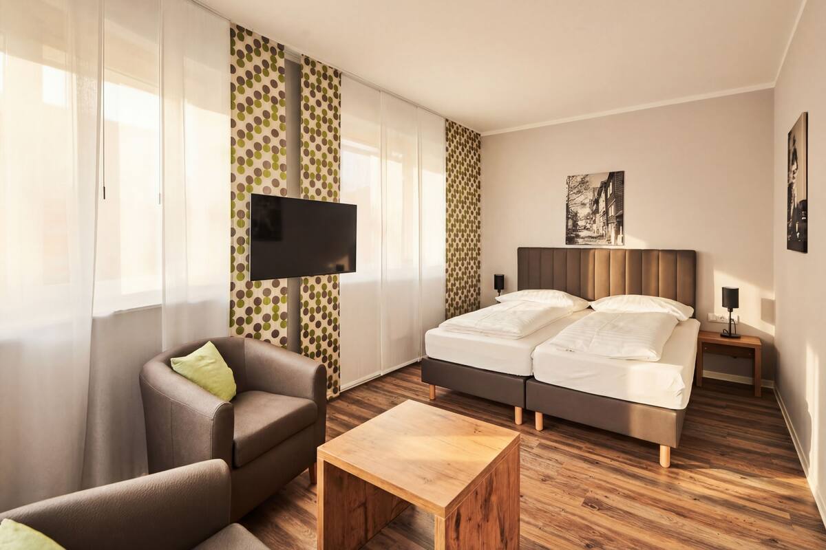 A hotel room with a bed, a TV, a chair, a bedside table, and curtains.