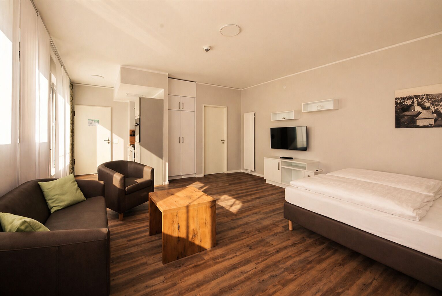 Una habitación de hotel moderna con sofá, una mesa de centro de madera, cama, televisor y armario.