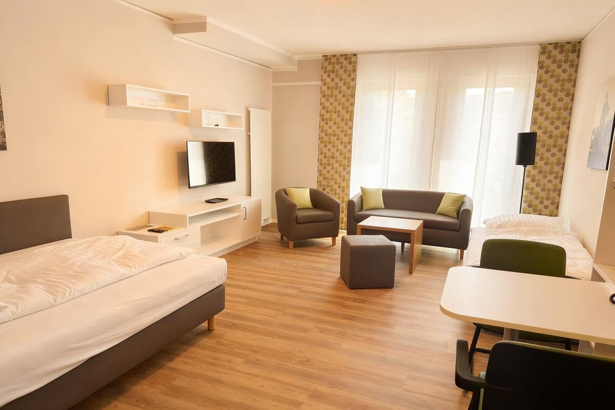 A hotel room with a bed, a TV, a sofa, a dining table, and a chair.