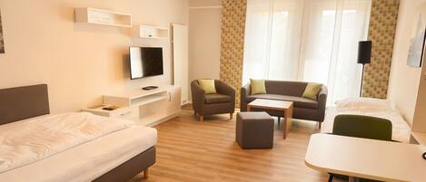 A hotel room with a bed, a TV, a sofa, a dining table, and a chair.