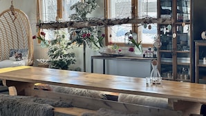 A cozy room with a wooden dining table, a decorative branch with ornaments, a small Christmas tree, and a glass cabinet with dishes. - Jokimaja Boutique Hotel (Kittila)