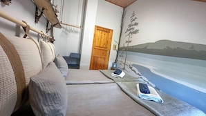 A room with a bed, a wooden door, a wall mural, and a small shelf with a basket. - Jokimaja Boutique Hotel (Kittila)