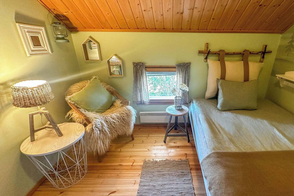 A cozy room with a bed, a chair, a small table, and a window with curtains.