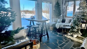A cozy room with a stone floor, a dining table with stools, a sofa with a fur throw, and a Christmas tree. - Jokimaja Boutique Hotel (Kittila)