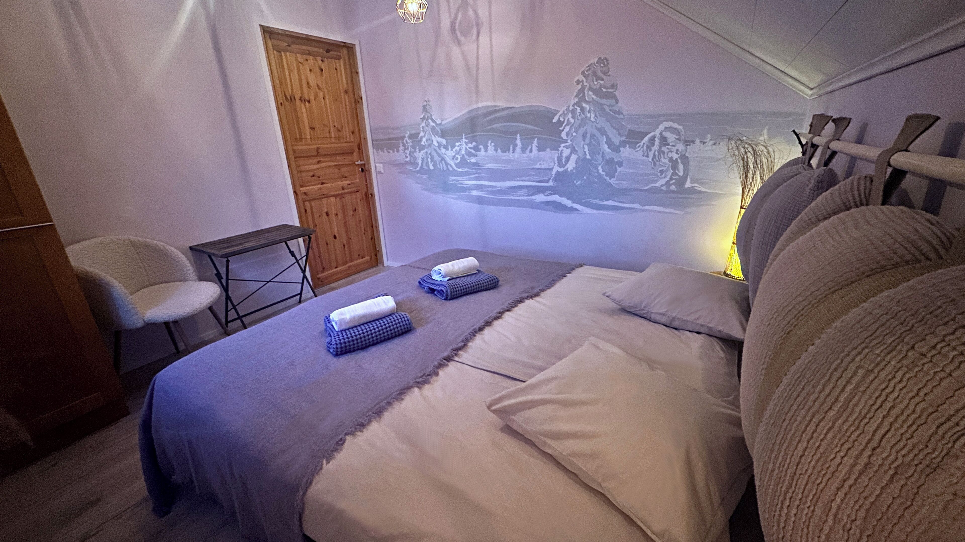 Un dormitorio con una cama, una mesita, una silla y un mural en la pared.