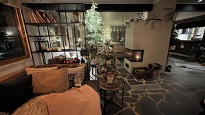 A cozy living room with a fireplace, a Christmas tree, and a stone floor. - Jokimaja Boutique Hotel (Kittila)