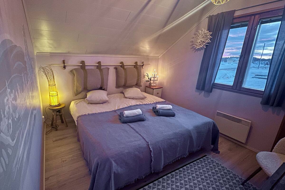 A cozy bedroom with a bed, bedside lamps, a nightstand, and a window with a view of a snowy landscape.