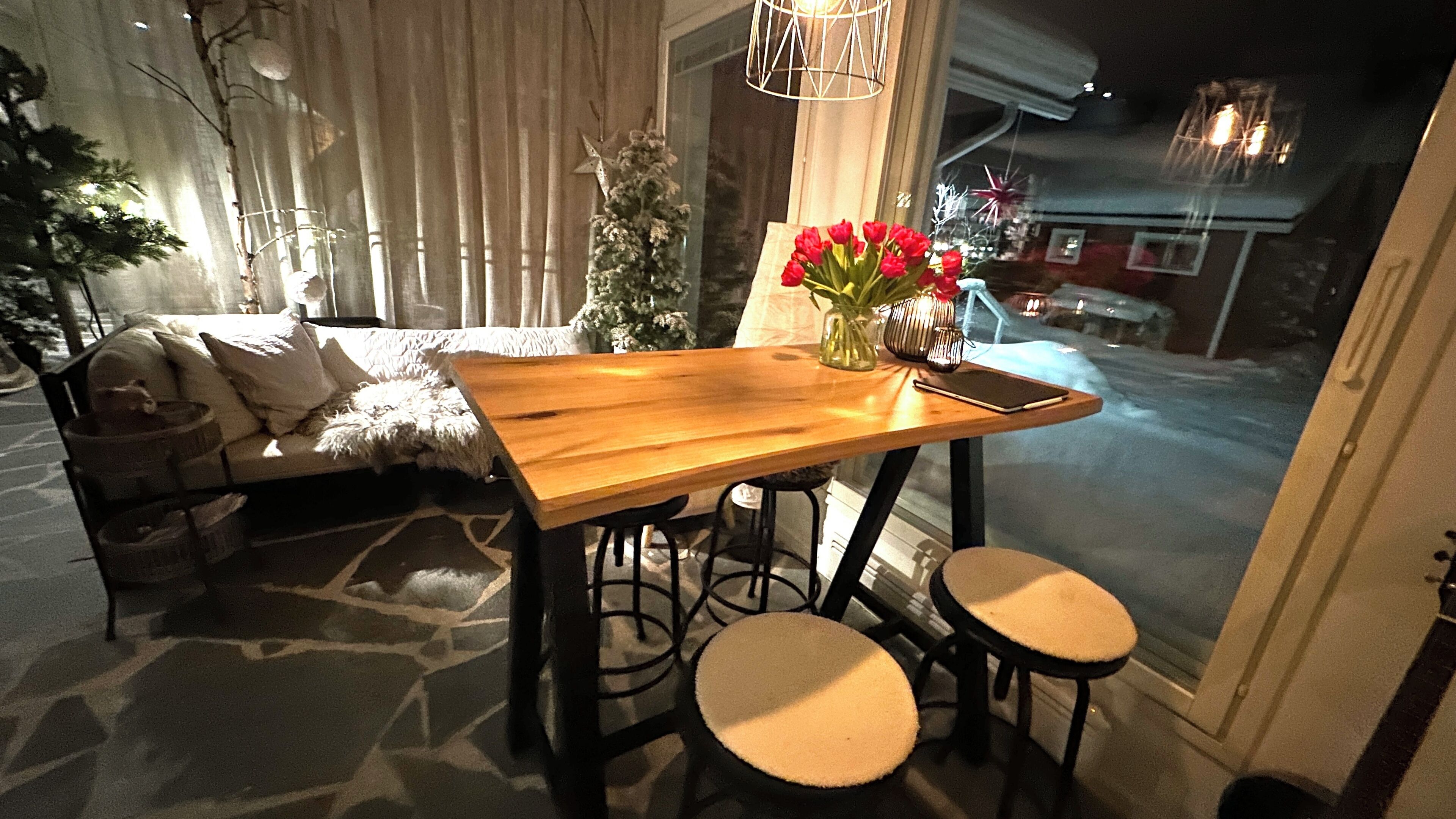Ein gemütlicher Essbereich mit Holztisch, zwei Hocker und einer Vase mit roten Blumen.