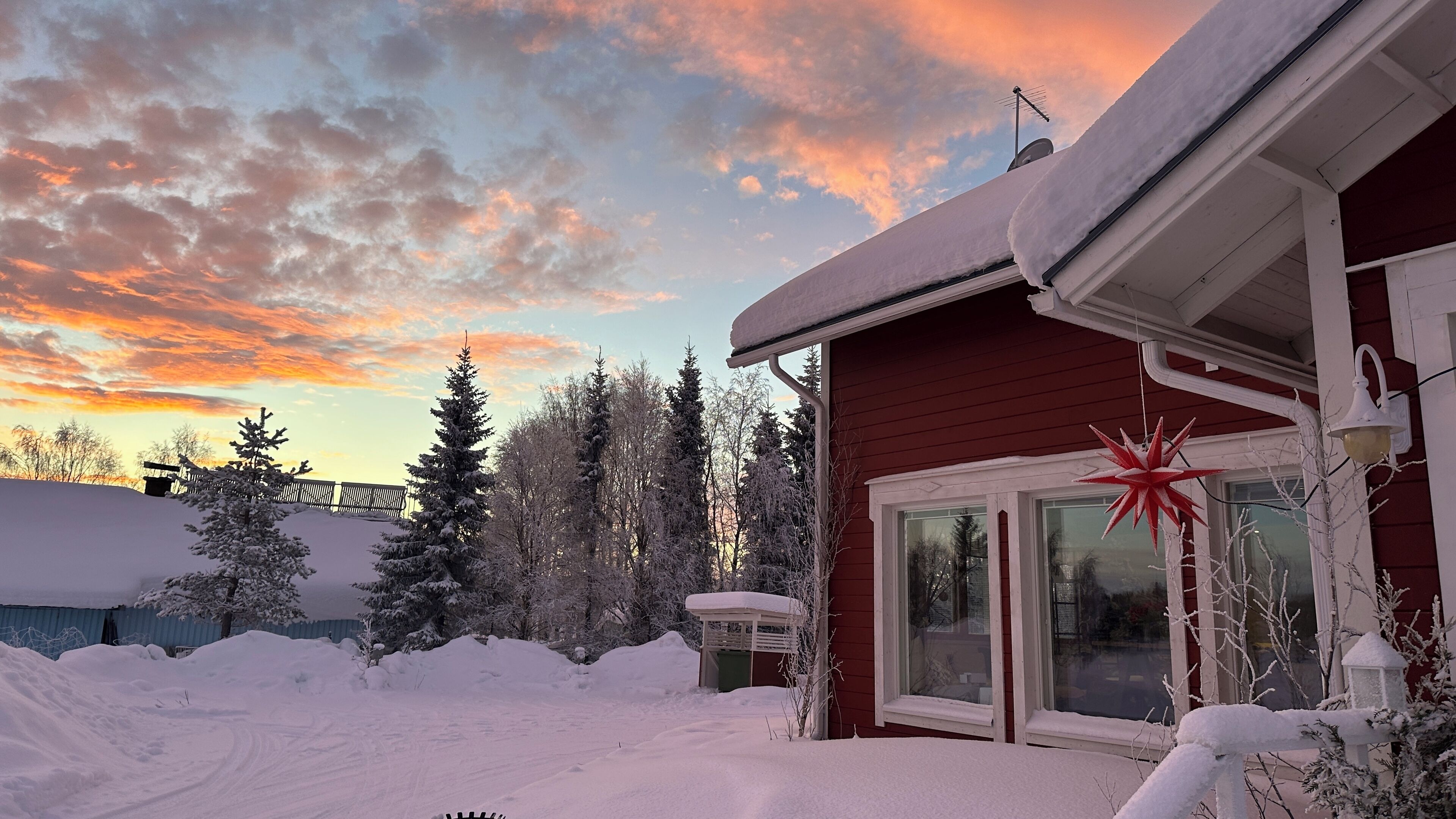 A house with a red exterior, a covered porch, and a snow-covered yard.