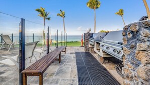 An outdoor patio with a stone grill, seating area, and a view of the ocean. - Kihei Surfside, #403 1 Bedroom Condo (Kihei)