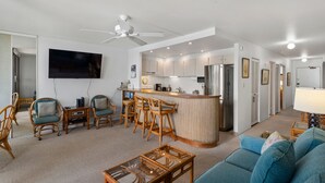 A modern living room with a sofa, chairs, a coffee table, and a television. - Kihei Surfside, #403 1 Bedroom Condo (Kihei)