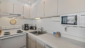 A compact kitchen with white cabinets, a stove, a sink, a coffee maker, and a microwave. - Kihei Surfside, #403 1 Bedroom Condo (Kihei)
