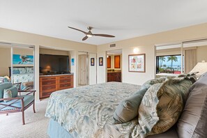 A bedroom with a bed, a desk, a chair, a ceiling fan, and a view of the ocean through a window. - Wailea Elua, #2107 2 Bedroom Condo (Kihei)