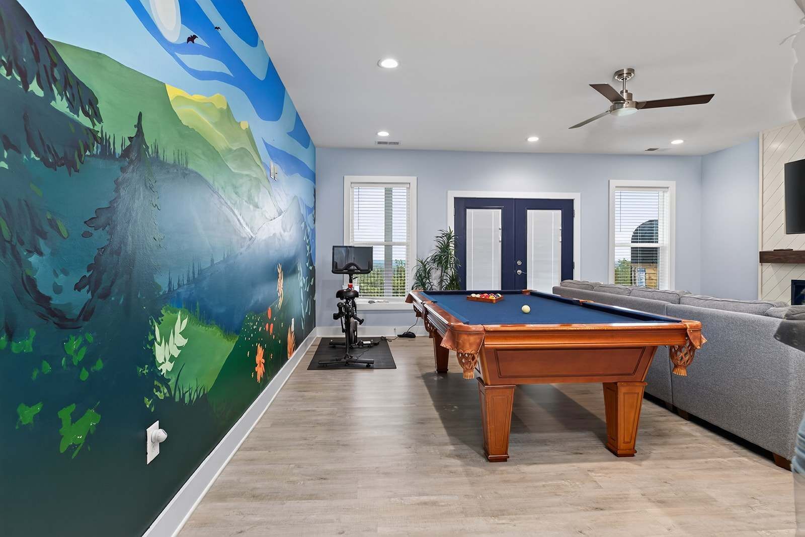 A pool room with a pool table, a ceiling fan, and a large mural on the wall.