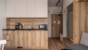A compact kitchen with wooden cabinets, a black countertop, a coffee maker, a toaster, and a microwave. - RentPlanet - Studio Zwycięska (Wroclaw)