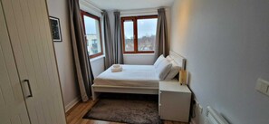 Un dormitorio con cama, mesita de noche, cortinas en la ventana y vistas al exterior.