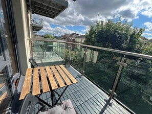 Ein Balkon mit Glasgeländer, einem Holztisch und einem Stuhl.