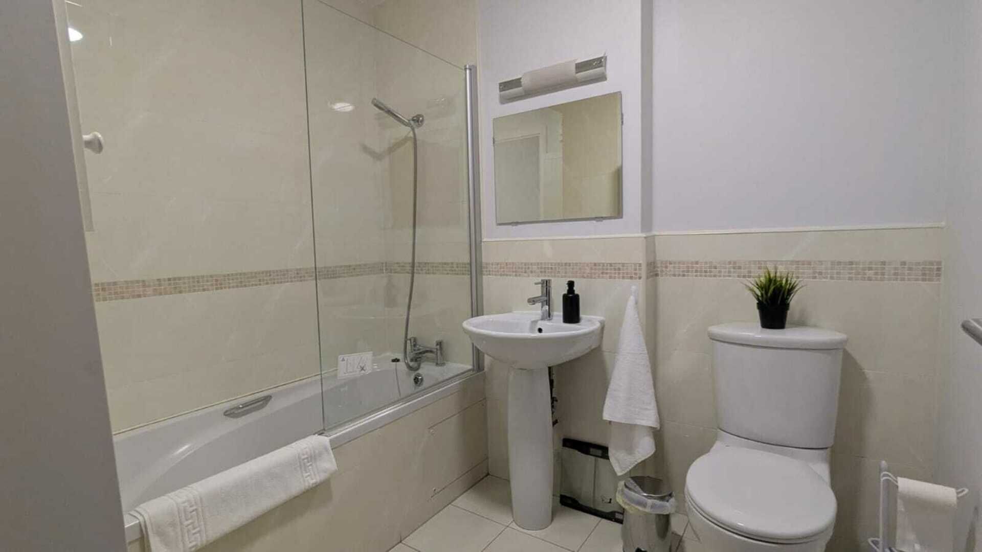 A bathroom with a glass-enclosed shower, a pedestal sink, a toilet, and a mirror above the sink.