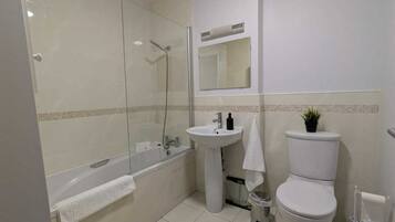 A bathroom with a glass-enclosed shower, a pedestal sink, a toilet, and a mirror above the sink.