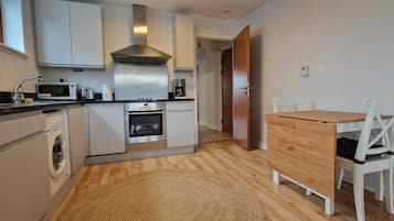 A compact kitchen with a washing machine, microwave, oven, and a wooden dining table with chairs.