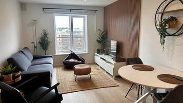A modern living room with a sofa, a dining table, a bean bag, and a TV on a white cabinet.