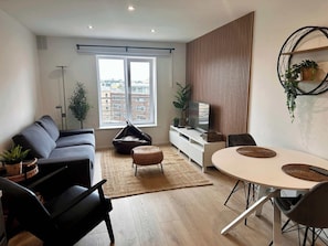 A modern living room with a sofa, a dining table, a bean bag, and a TV on a white cabinet.