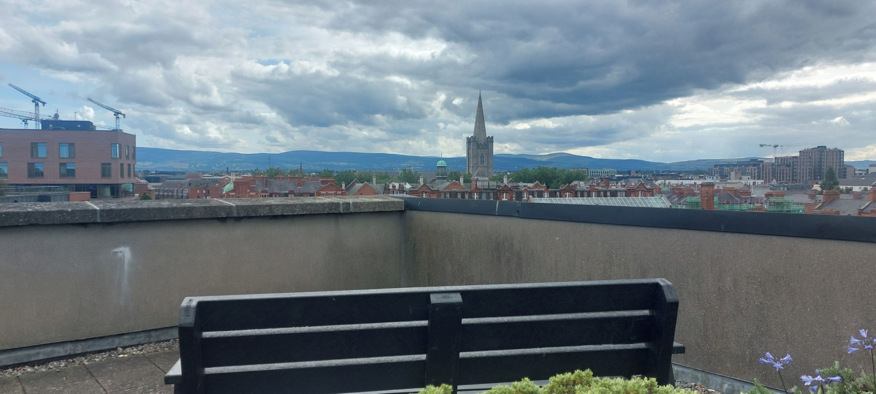 Un balcon avec un banc, d’où l’on peut admirer un panorama sur la ville, avec ses bâtiments et une tour imposante.