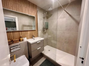 A modern bathroom with a vanity, sink, mirror, shower, and a toilet.