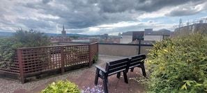 Un jardin sur le toit, avec un banc, une clôture en bois et une vue sur le paysage urbain, avec ses bâtiments et le clocher d’une église.