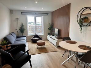A modern living room with a sofa, a dining table, and a TV on a white cabinet.
